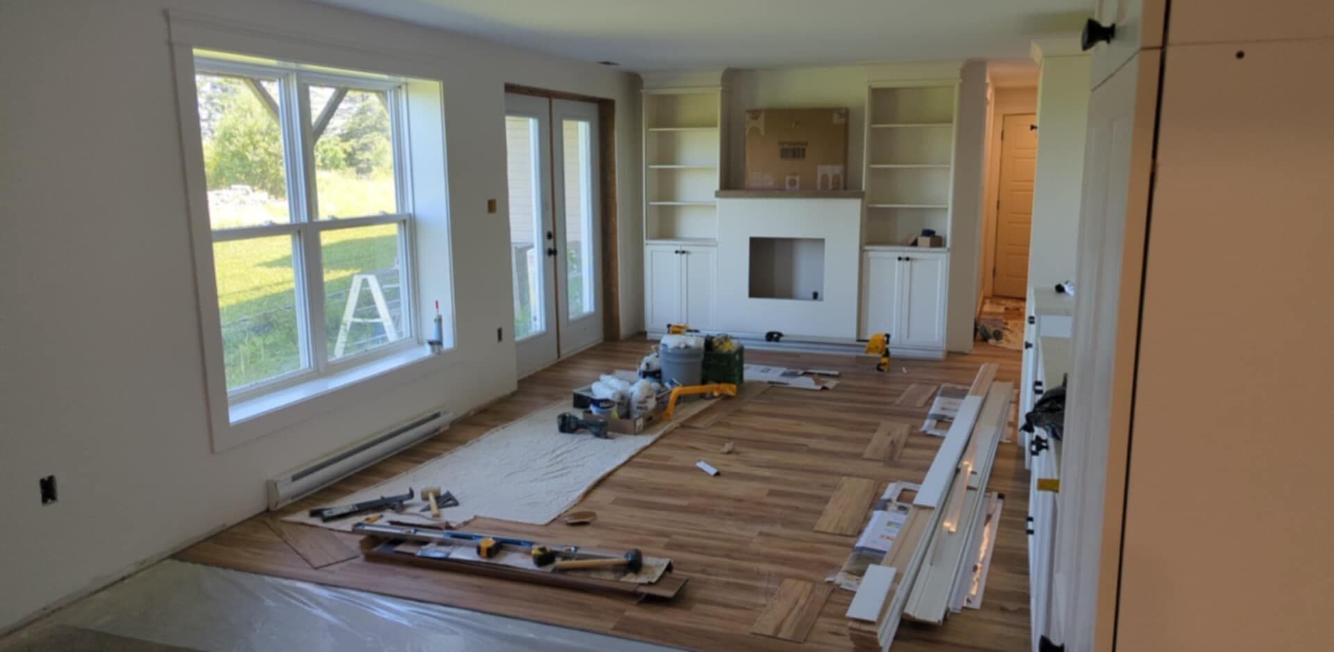 Basement living area during renovation, with built-in shelves, wood flooring, and finishing materials