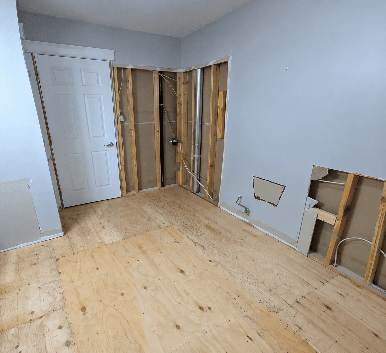 Room mid-renovation with framed walls and a plywood subfloor, before finishing