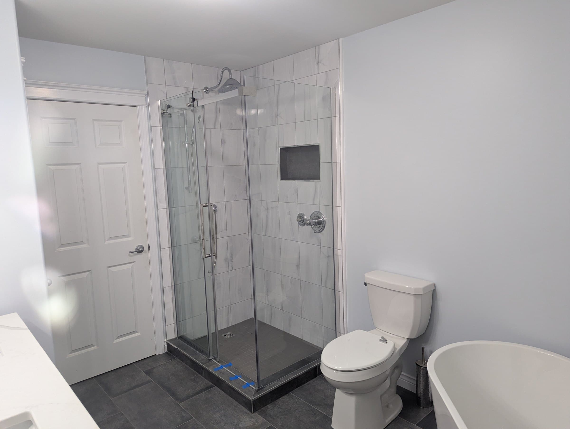 Glass shower with marble-look wall tile beside the tub and toilet in the Taylor bathroom