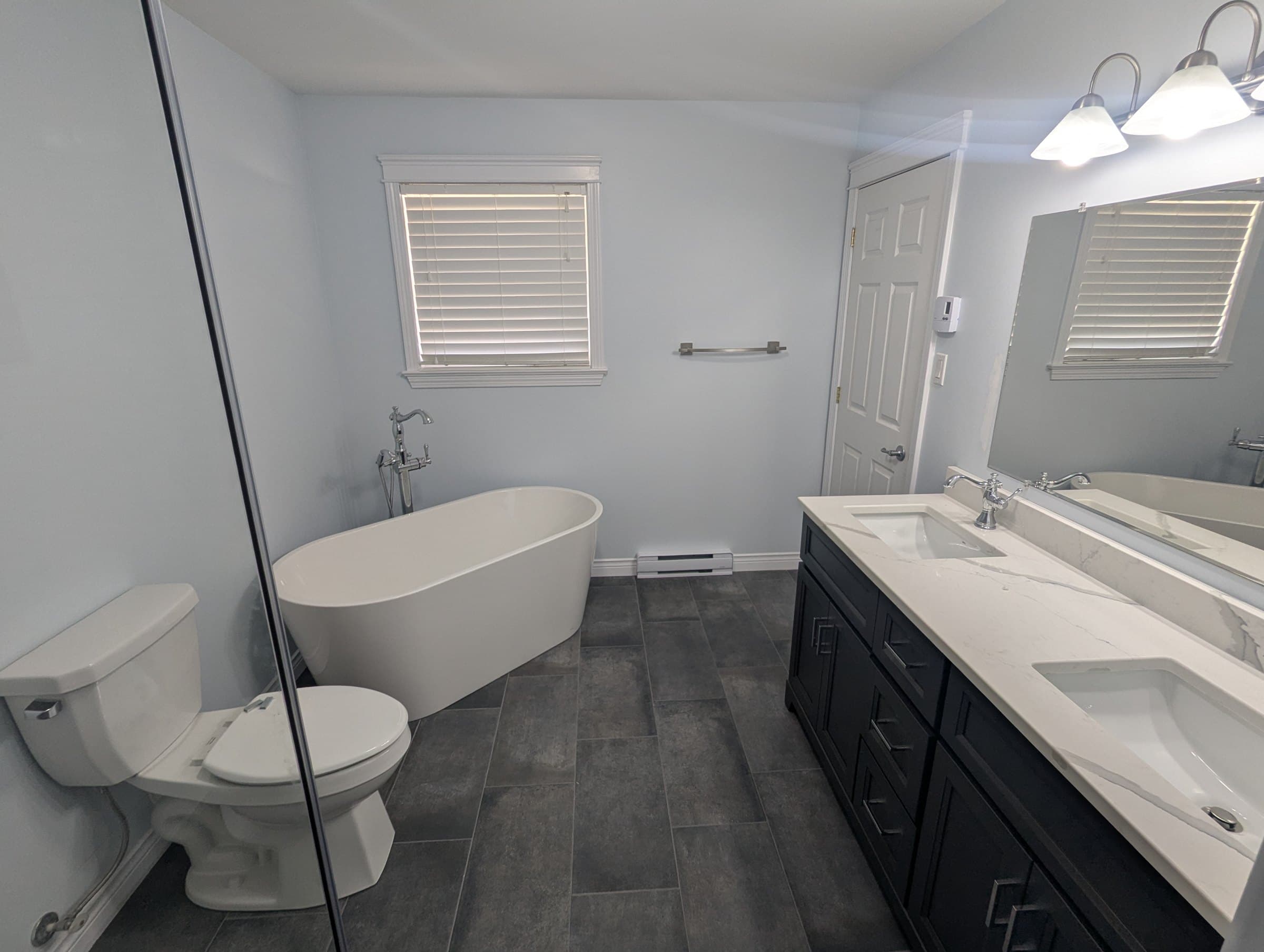 Bathroom with a freestanding tub, double sink vanity, and dark floor tile