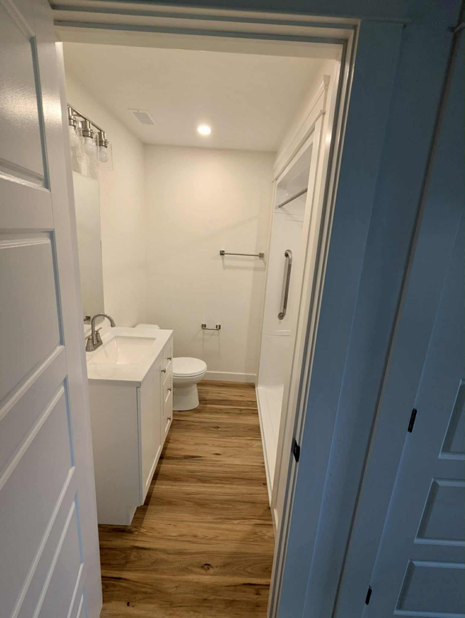 Finished compact bathroom viewed through the doorway, with a white vanity, shower enclosure, and wood-look flooring