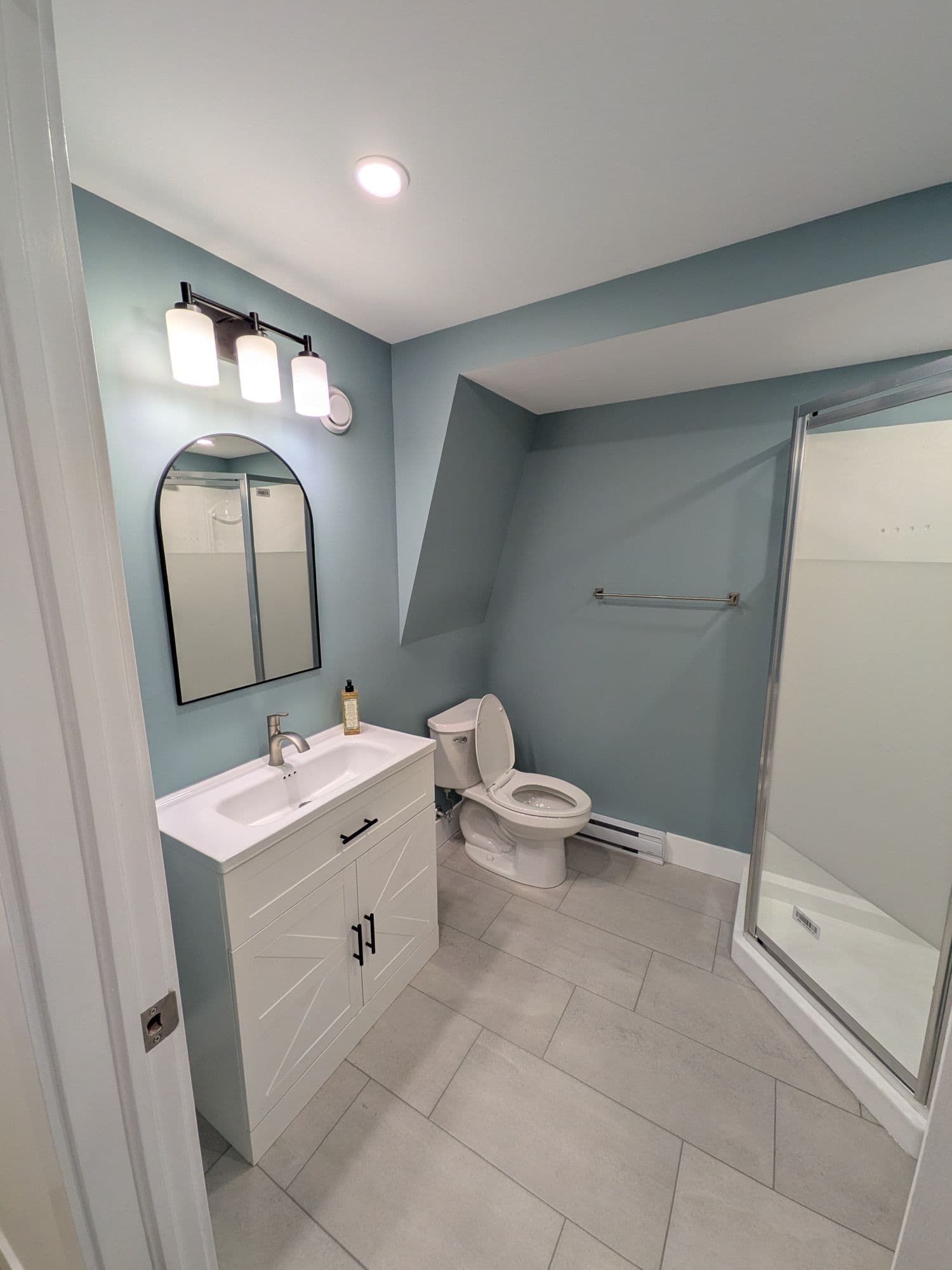 Finished bathroom with blue walls, a white vanity, grey tile flooring, and a glass shower enclosure
