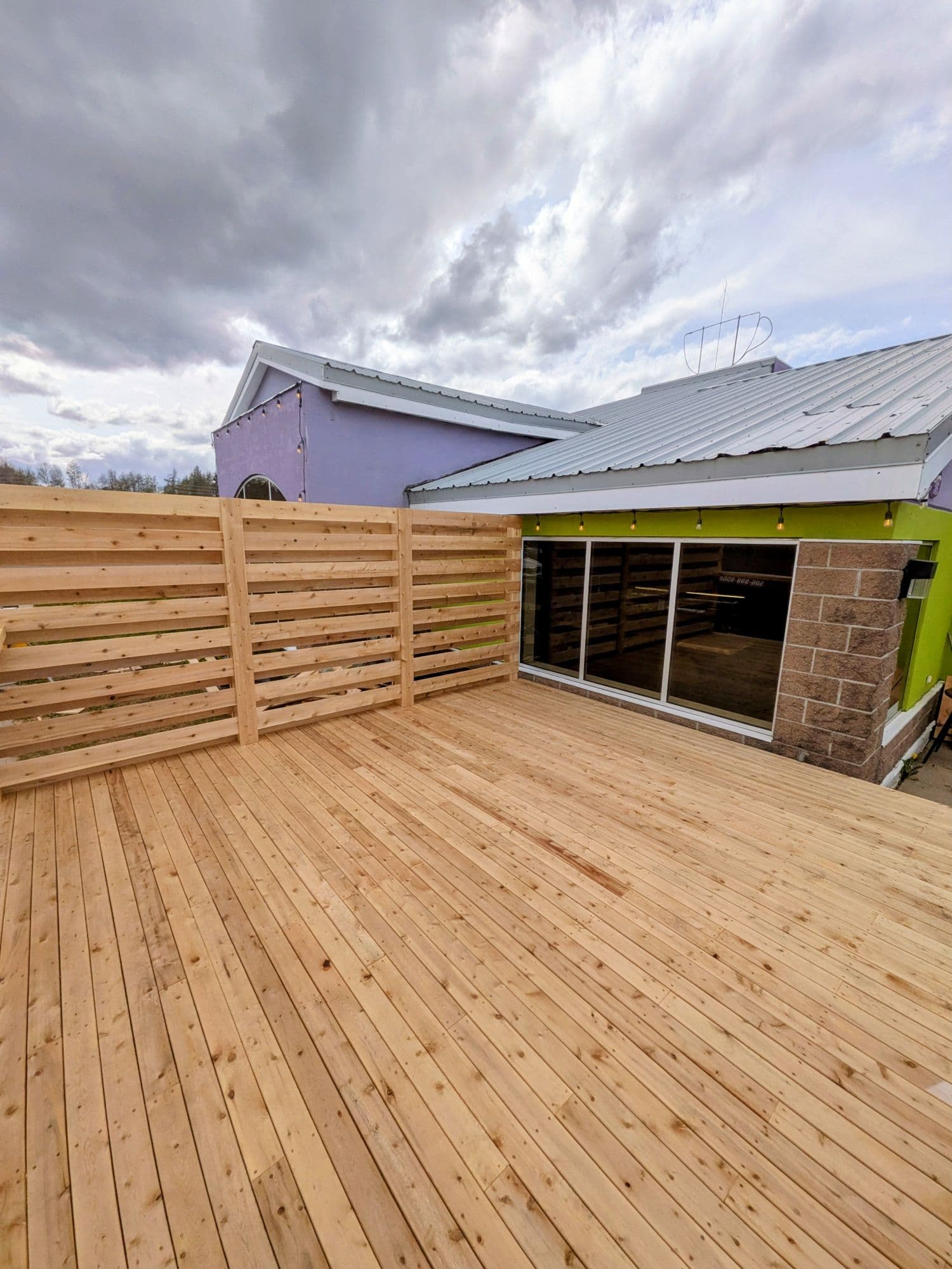 Finished cedar deck with a slatted privacy wall next to a commercial building