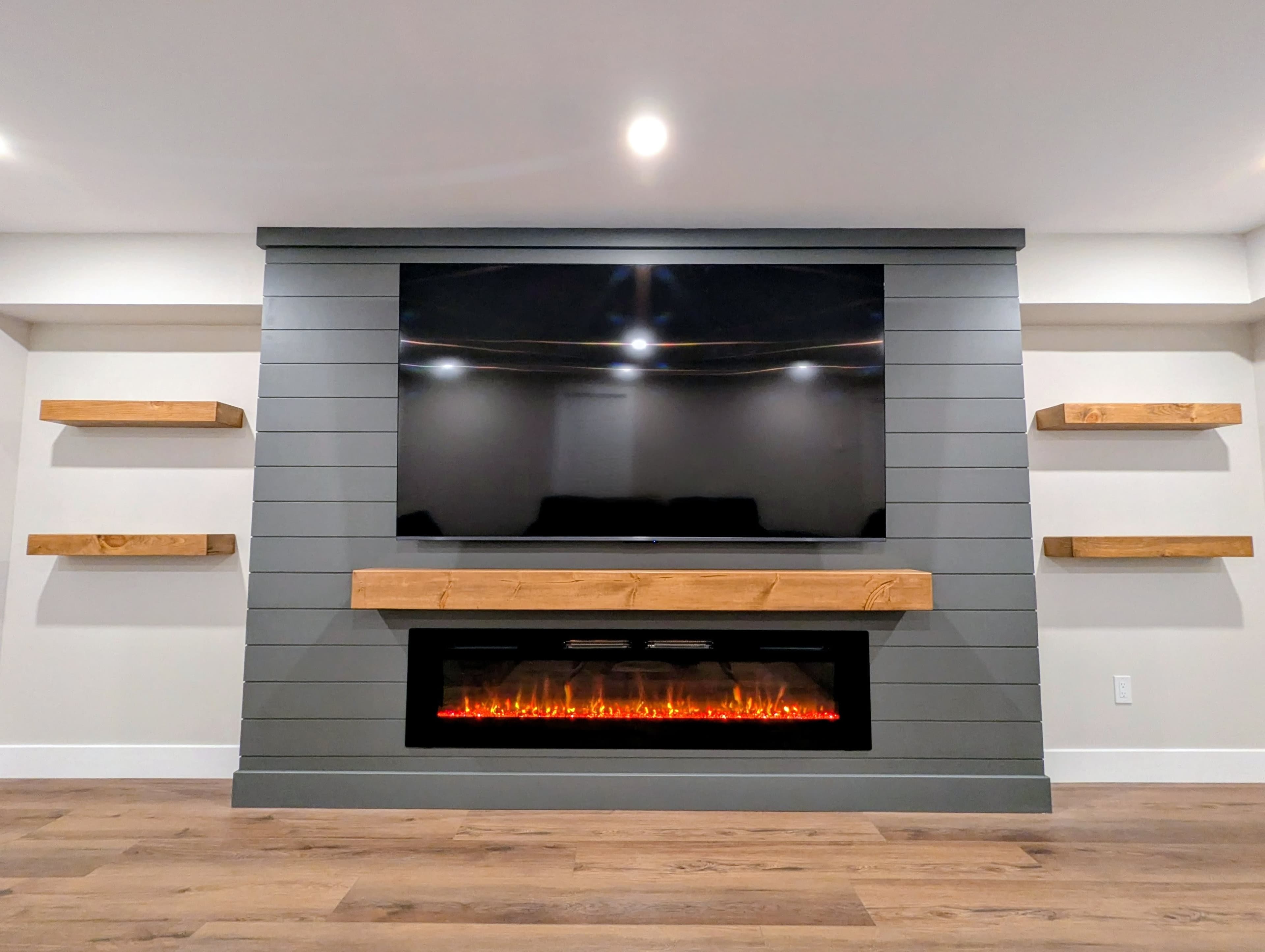 Close-up of the basement family room's media wall with a mounted TV, wood mantel, and built-in fireplace