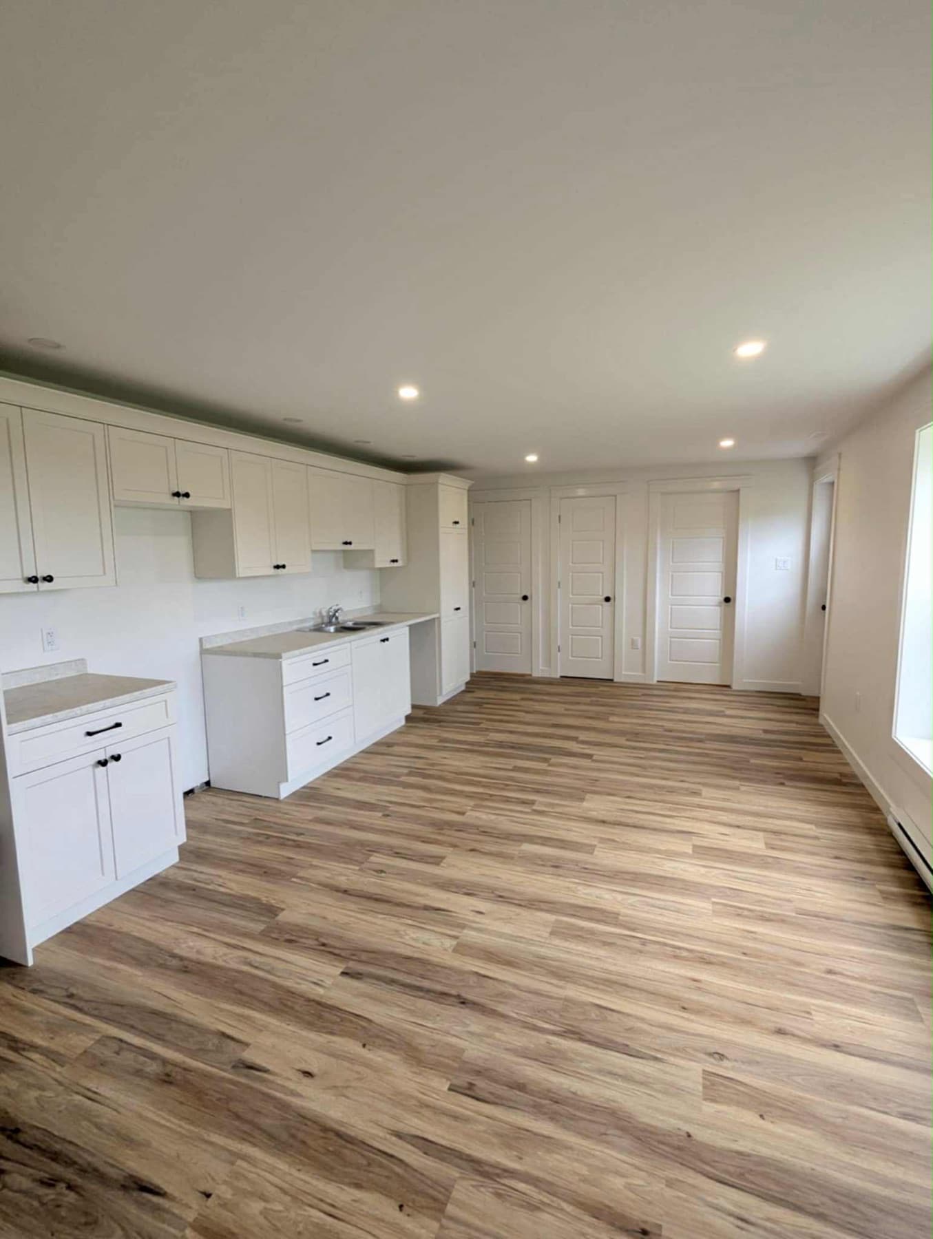 Finished open-plan interior with white kitchenette cabinetry, wood-look flooring, and recessed lighting